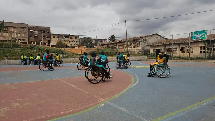 Vue large du terrain extérieur pendant un match de basket fauteuil, sous un ciel nuageux.
