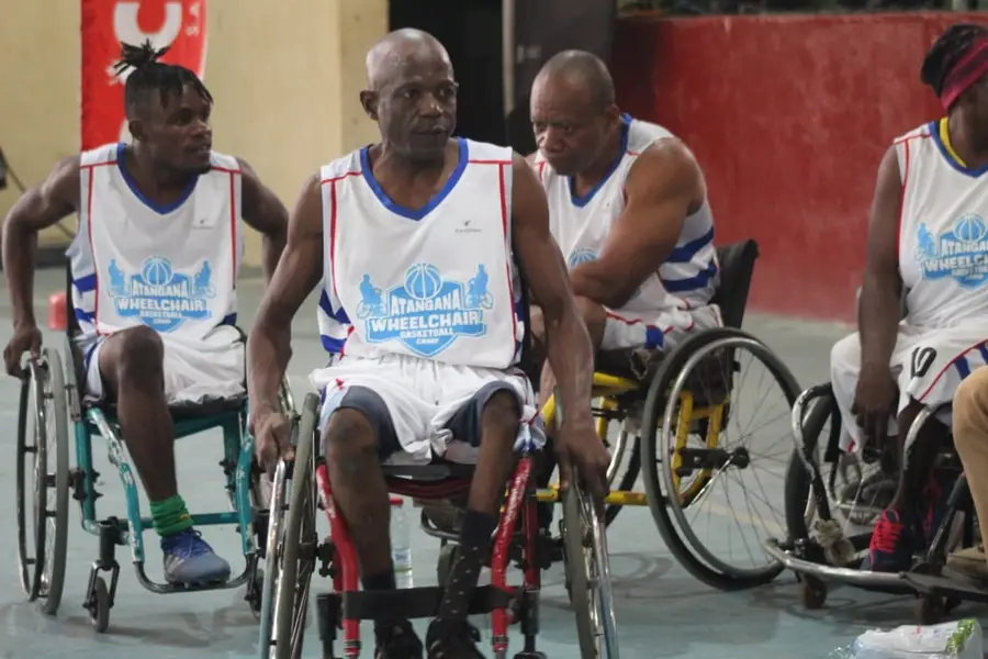 Trois joueurs en maillots blancs du camp Atangana côte à côte en fauteuil de sport.