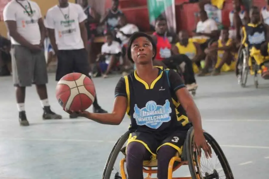 Une joueuse en fauteuil, maillot noir numéro 3 du camp Atangana, tient le ballon d’une main.